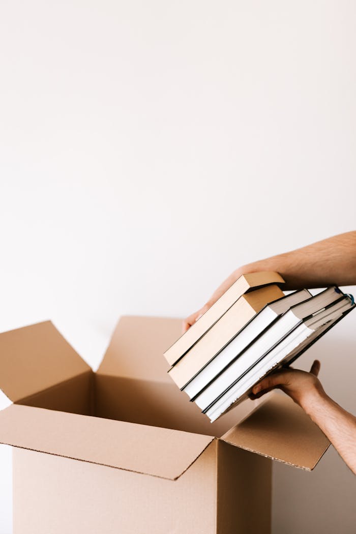 Person organizing and packing books into a cardboard box, preparing for relocation.